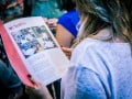 Foto mostra mulher segurando material de apoio do Criativos da Escola