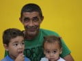 Foto mostra homem sorrindo junto de duas crianças