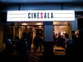 Foto mostra Cinesala com várias pessoas dentro e uma placa iluminada escrito "CineSala"