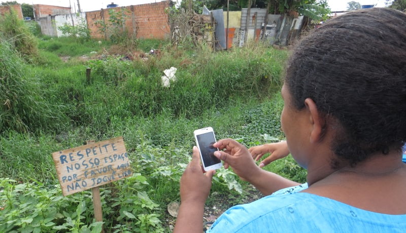 Foto de mulher tirando foto com o celular de uma placa escrito "Respeite nosso espaço, por favor, não jogue lixo".