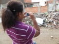 Foto mostra mulher tirando foto com o celular de pilha de entulhos