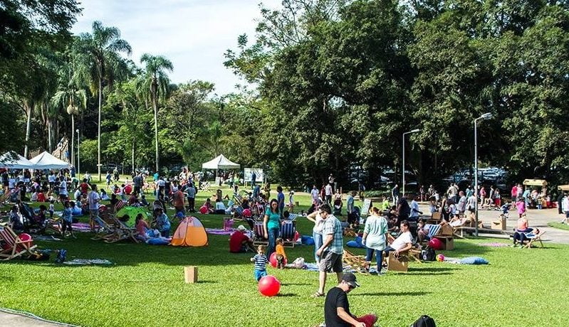 Parque com uma extensa área de gramado verde e pessoas circulando pelo local.