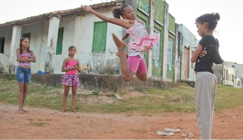 Foto de quatro meninas negras brincando de pular corda em rua de terra