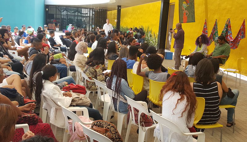 Público do evento que debateu o preconceito racial na atualidade sentado em cadeiras, enquanto um homem fala na frente.