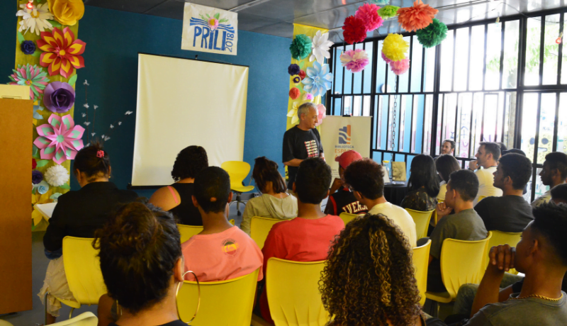 Foto da festa literária mostra auditório com pessoas sentadas em cadeiras amarelas assistindo a uma palestra