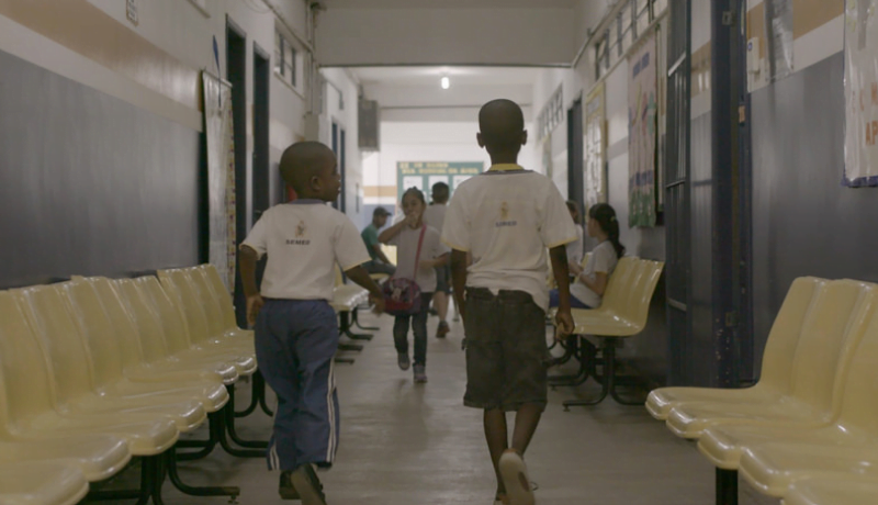 Foto de uma cena do 2º episódio da série "Corações e Mentes" mostra duas crianças de costas andando em corredor de escola