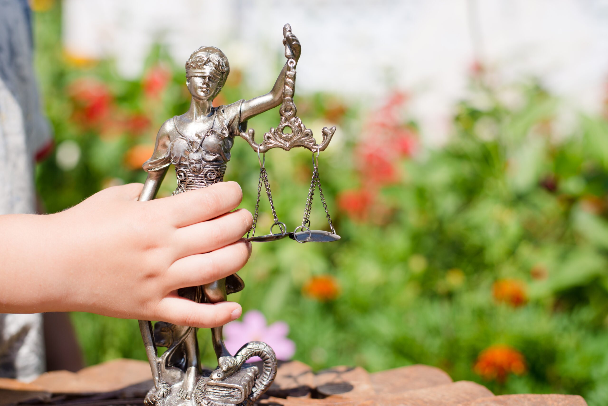 Foto mostra mão de criança segurando estátua da justiça