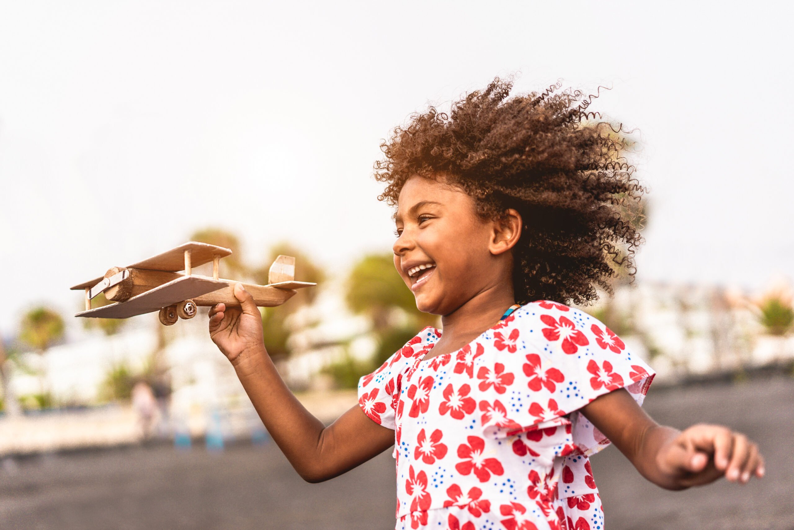 Foto de uma menina negra correndo com um aviãozinho de madeira em uma das mãos, em referência ao lançamento do material de apoio sobre educação antirracista.